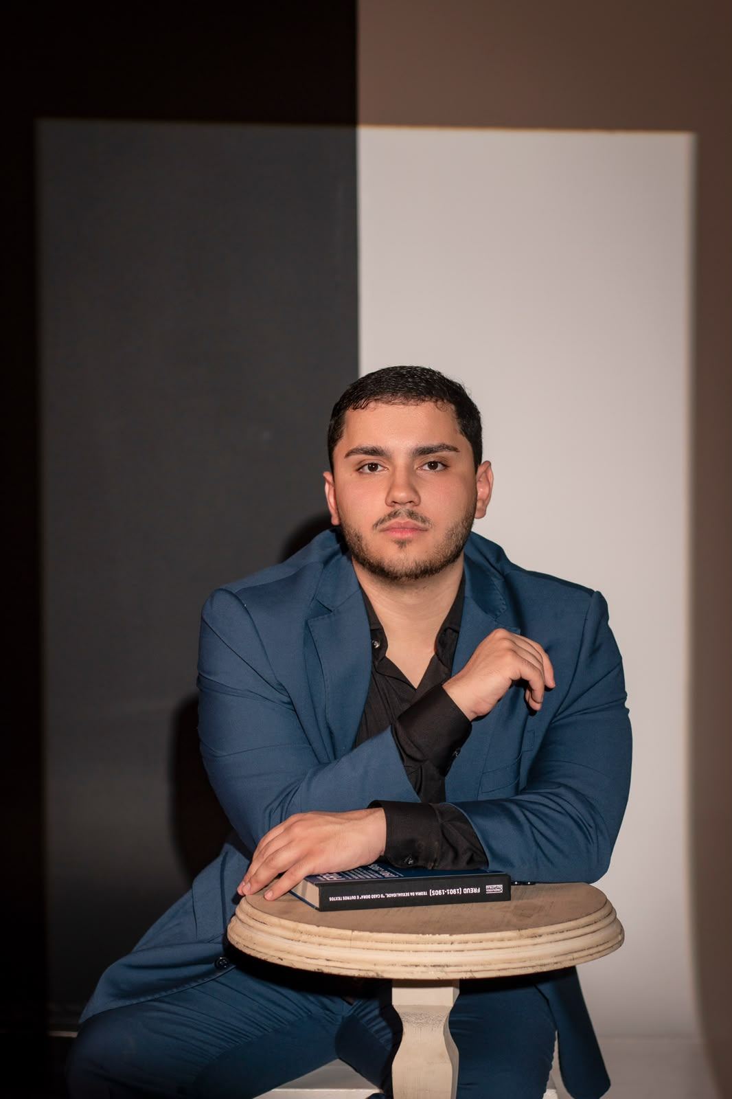 Marcus Trivellato, de blazer azul-marinho, apoiado em uma mesa com um livro de Freud